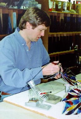Joseph E. Godek soldering stained glass dragons in his home studio